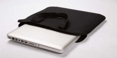 A silver laptop partially slides out of a sleek black carrying case resting on a plain white surface. The scene is minimalistic and functional, evoking a sense of simplicity and readiness.